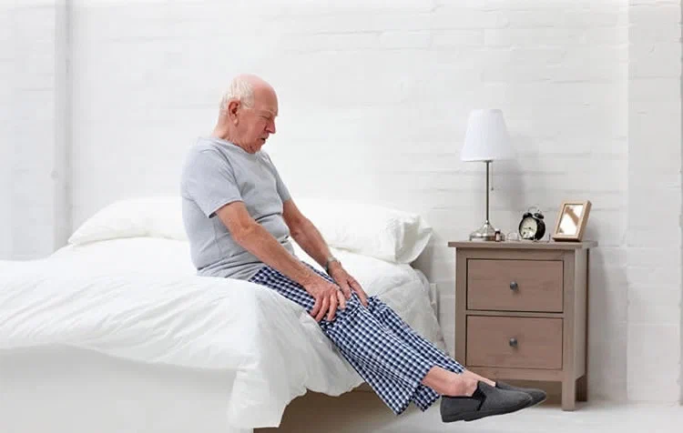 Senior beim Aufstehen aus dem Bett im Schlafzimmer